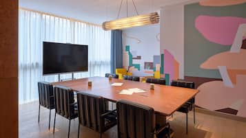 Een vergaderruimte met een grote tafel, stoelen, een flatscreen-tv en een kleurrijke abstracte muurschildering.