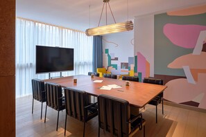 Un salón de conferencias con una gran mesa, sillas, un televisor de pantalla plana y un colorido mural abstracto en la pared.