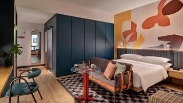 Une chambre d’hôtel moderne comprenant un canapé, une petite table ronde, un lit, une table de chevet et une grande œuvre d’art abstraite accrochée au mur.