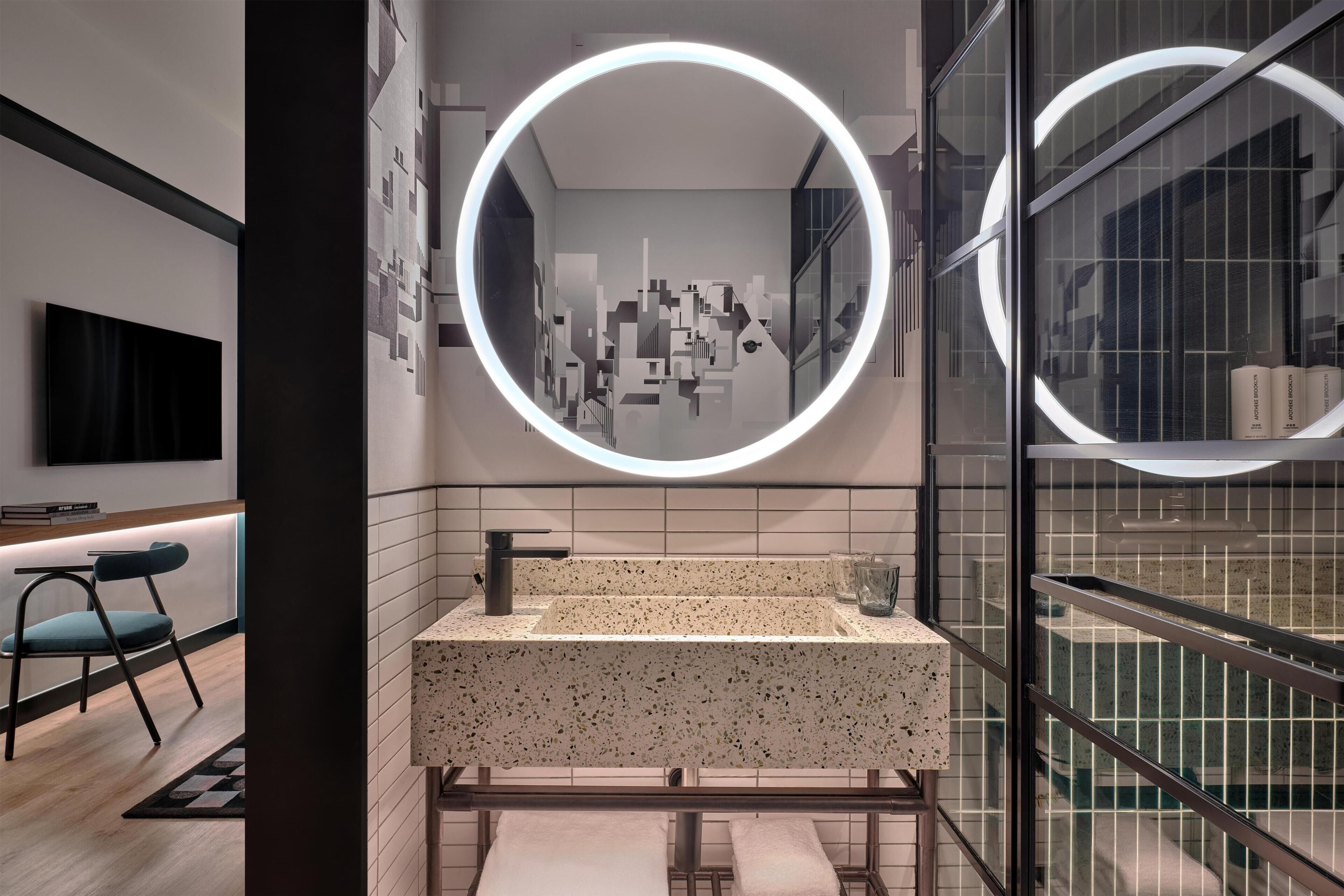 A modern bathroom with a round mirror, a sink with a speckled countertop, and a towel rack.