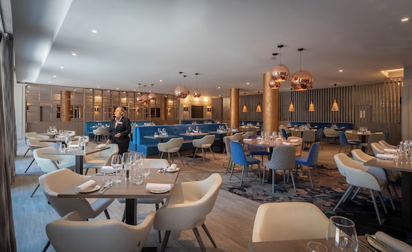 A modern restaurant interior with booths, round tables, and a waitstaff present.