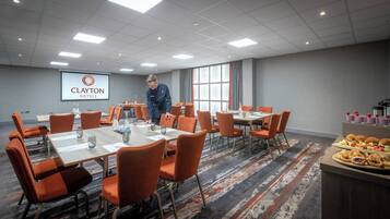 A conference room with tables, chairs, and a screen displaying 'CLAYTON HOTELS'.