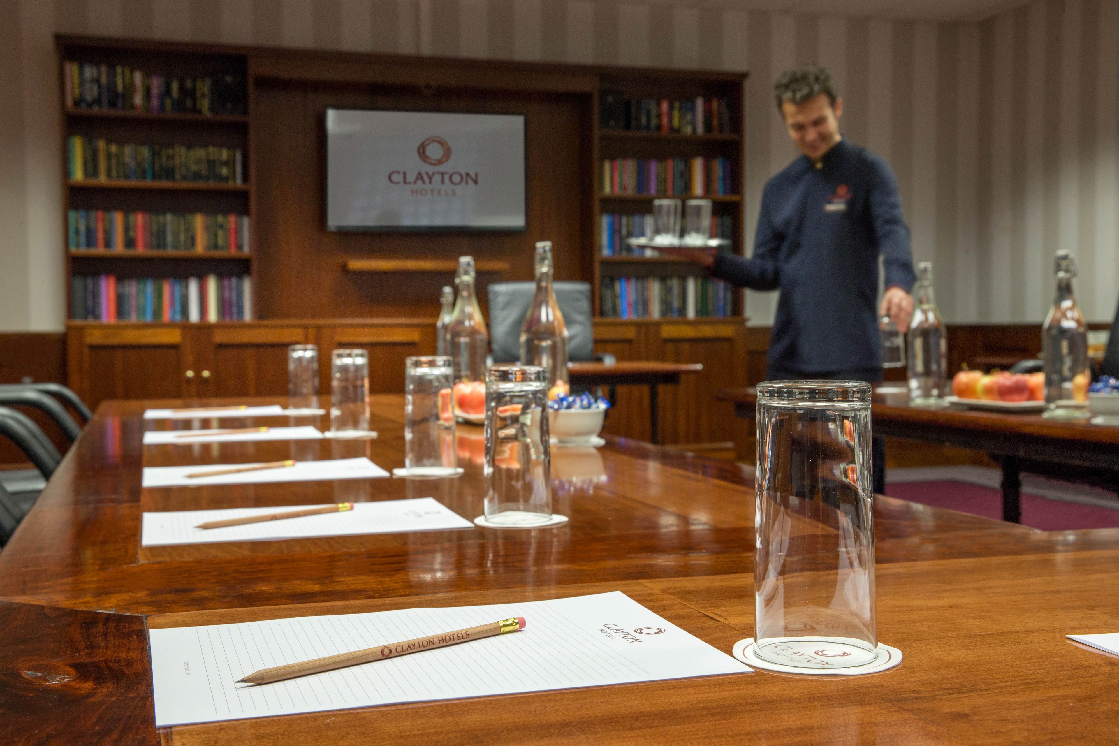 A conference table with lined papers, pens, and glass bottles in a hotel setting.