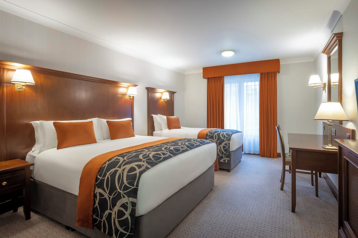 A hotel room with two beds, a desk, a chair, and a television.