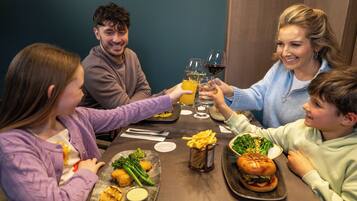Eine Familie isst in einem Restaurant. Auf dem Tisch stehen verschiedene Gerichte, darunter Burger und Pommes, sowie Getränke.