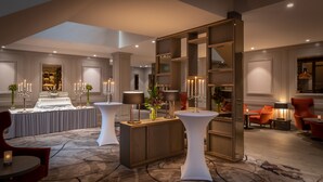 Un moderno vestíbulo de hotel con mostrador de recepción, zona de estar y detalles decorativos como candelabros y jarrones.