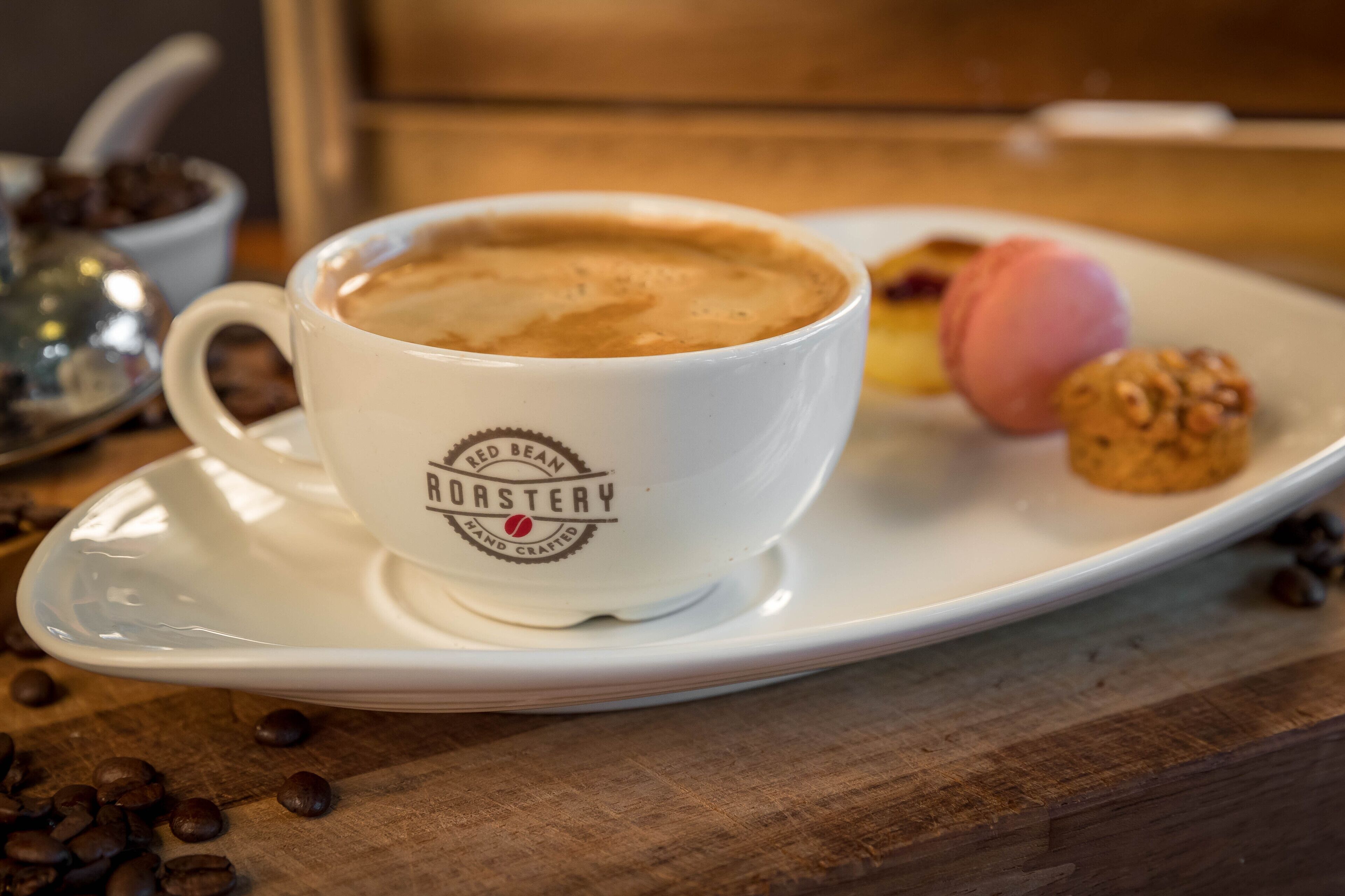 A cup of coffee on a saucer with a plate of pastries and a cookie.