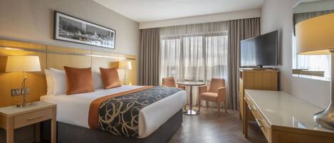 Habitación de hotel con cama, mesitas de noche, escritorio, silla, televisor y ventana con cortinas.