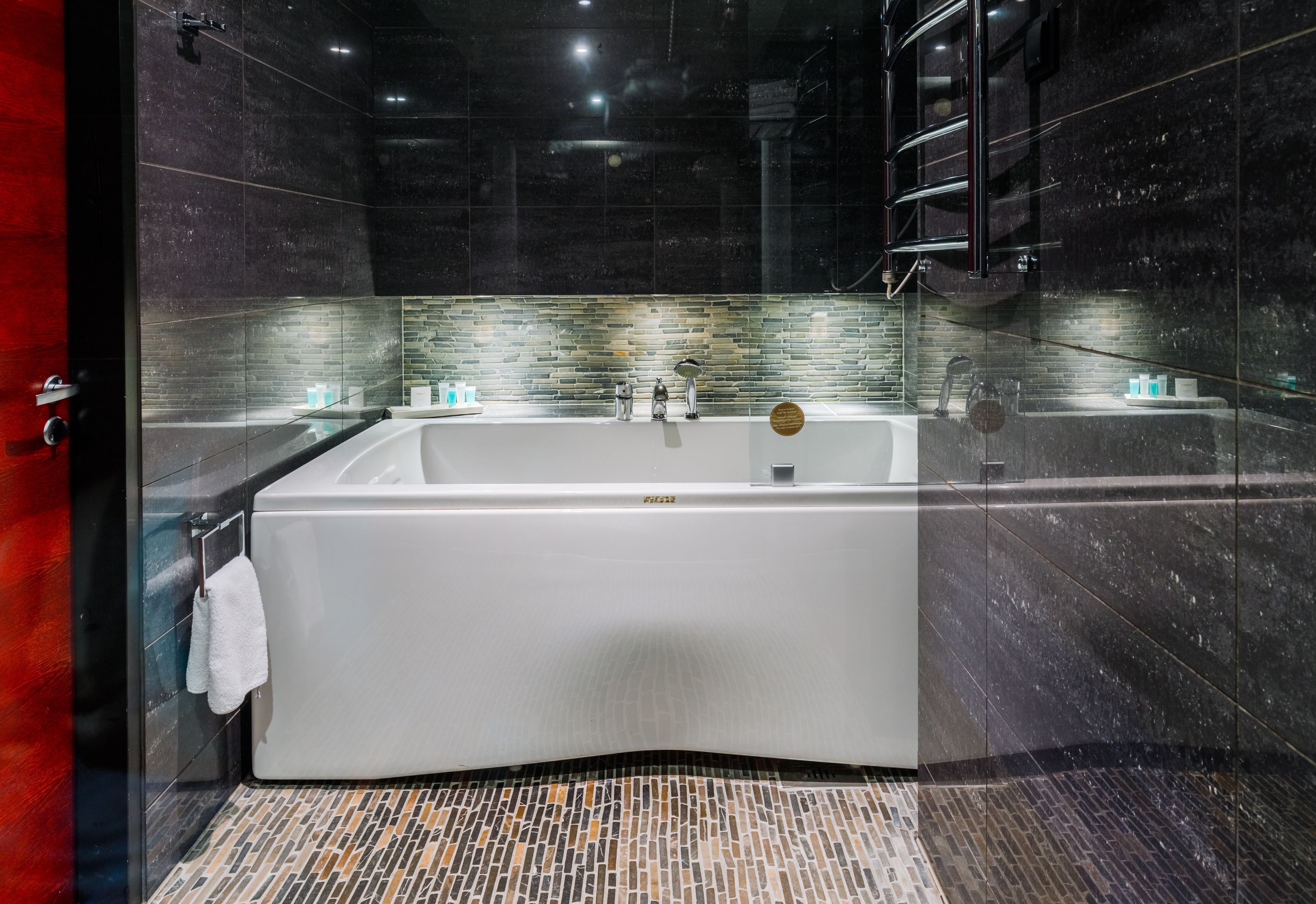 Une salle de bain moderne avec une grande baignoire, une douche à l’italienne en verre et un pare-baignoire en mosaïque.