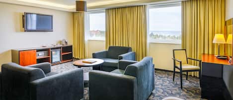 Habitación de hotel con zona de estar, televisión, minibar y vistas al exterior.