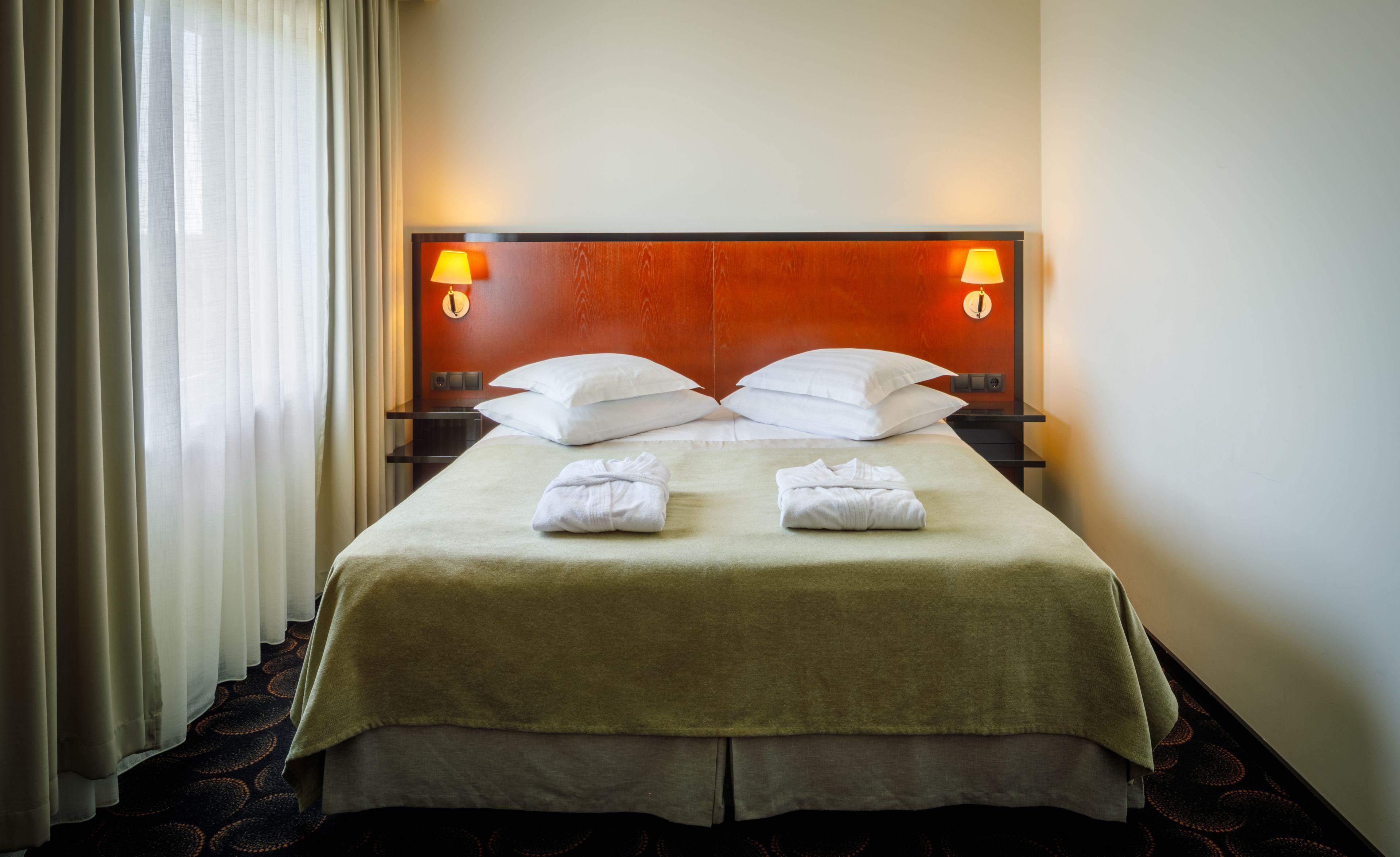 A hotel room with a large bed, two bedside lamps, and a window with curtains.
