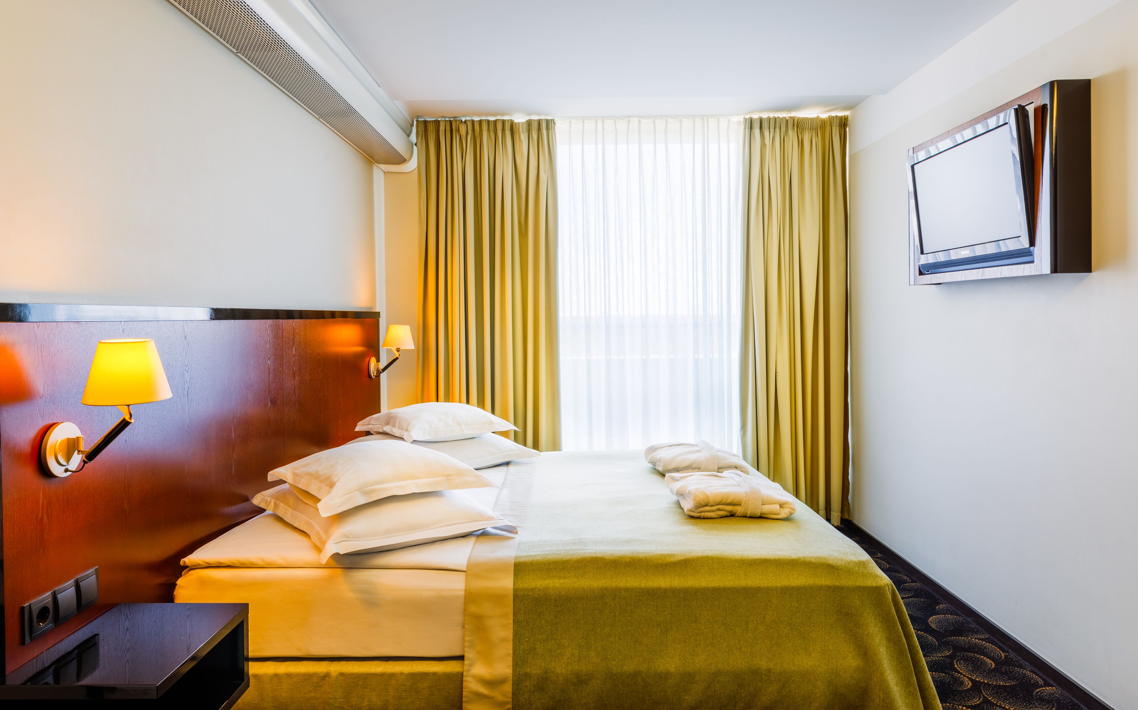 Une chambre d’hôtel avec un lit, une lampe de chevet, une télévision et une fenêtre avec des rideaux.