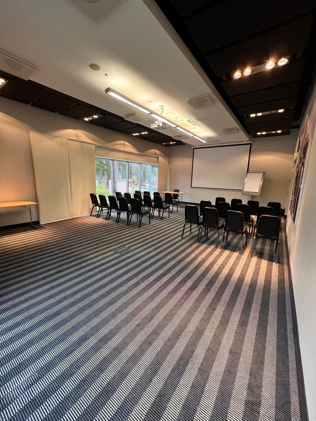 A conference room with a carpeted floor, black chairs, a projector screen, and a whiteboard.