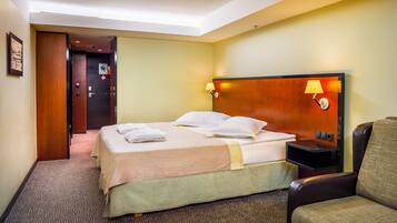 A hotel room with a bed, a chair, a nightstand, and a door.