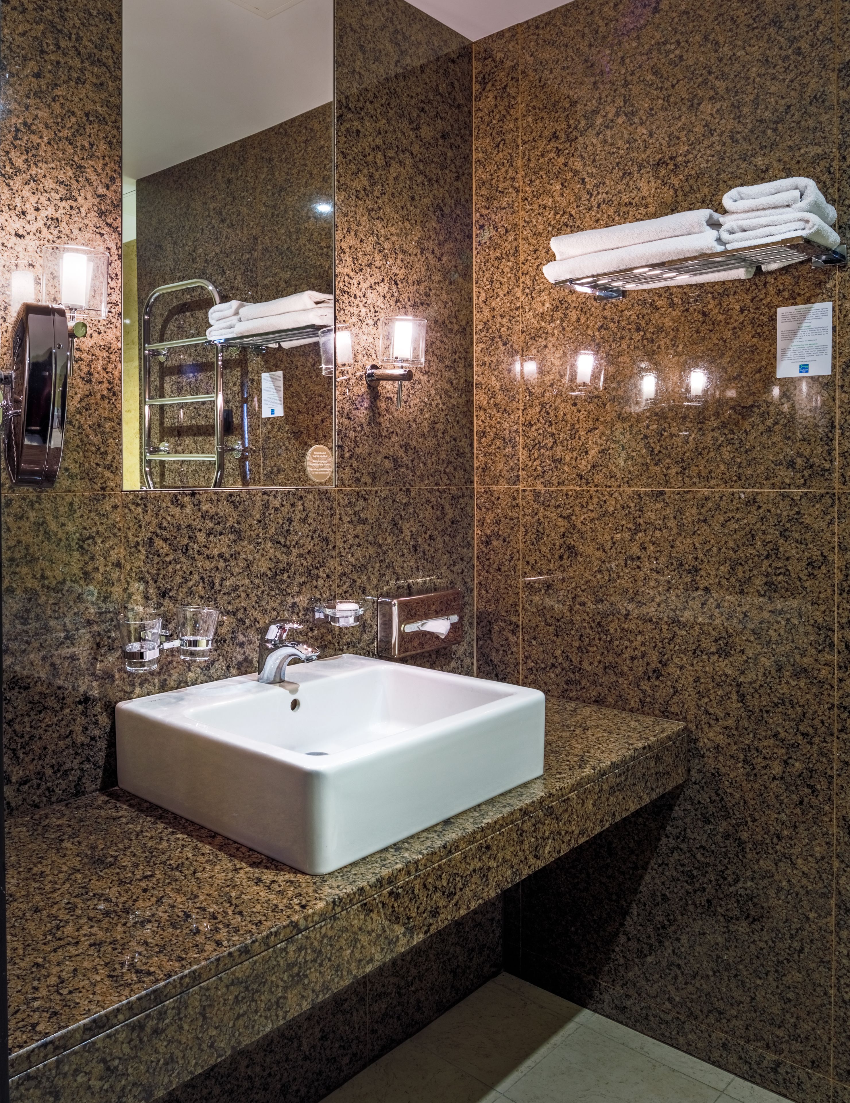 A modern bathroom with a granite countertop, a white sink, a mirror, and a towel rack.