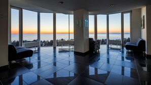 Un hall d’entrée spacieux, doté de grandes fenêtres offrant une vue sur la mer au coucher du soleil.