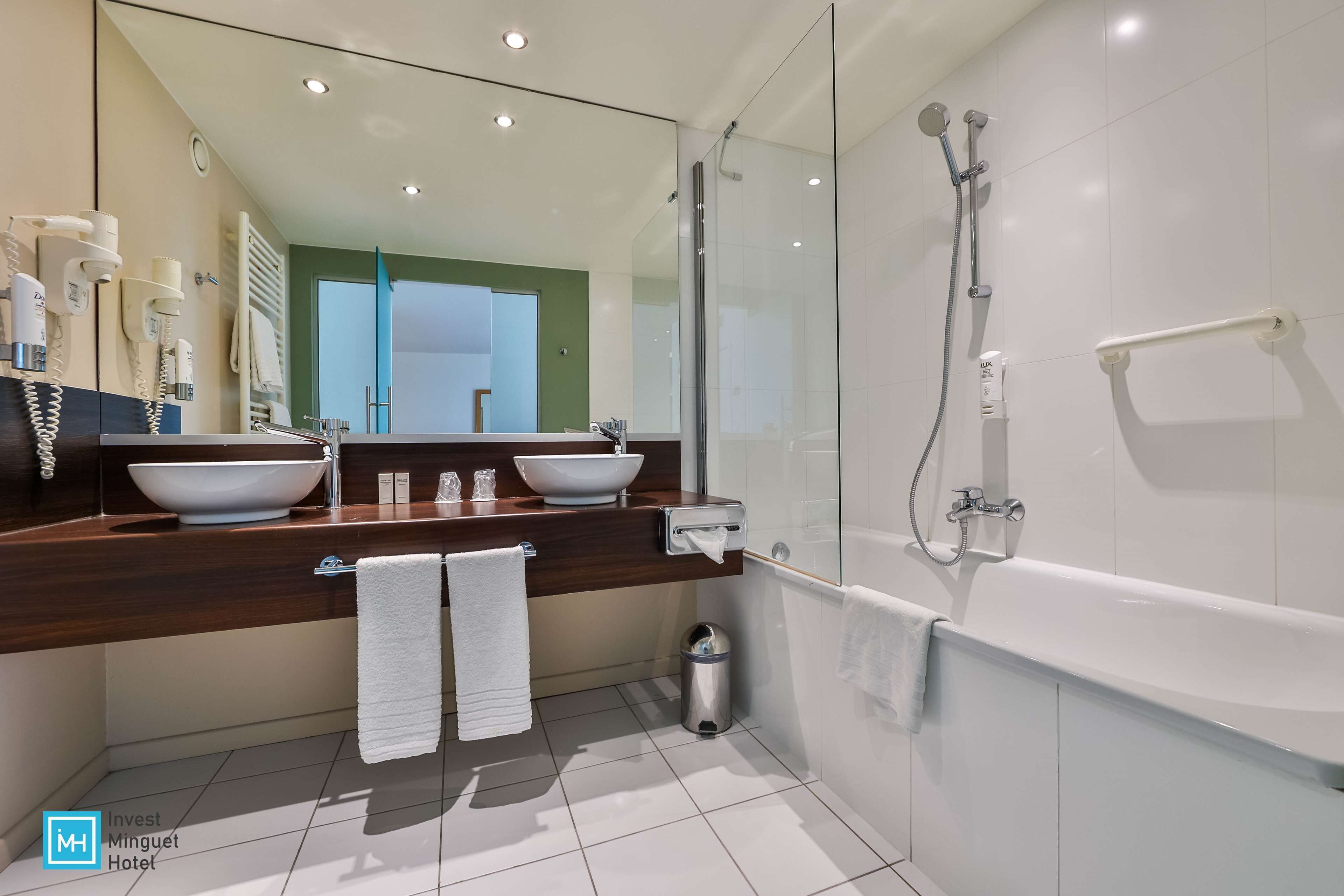 Un baño moderno con ducha envuelta en vidrio, una bañera blanca grande y un tocador de madera oscura con lavamanos blanco.