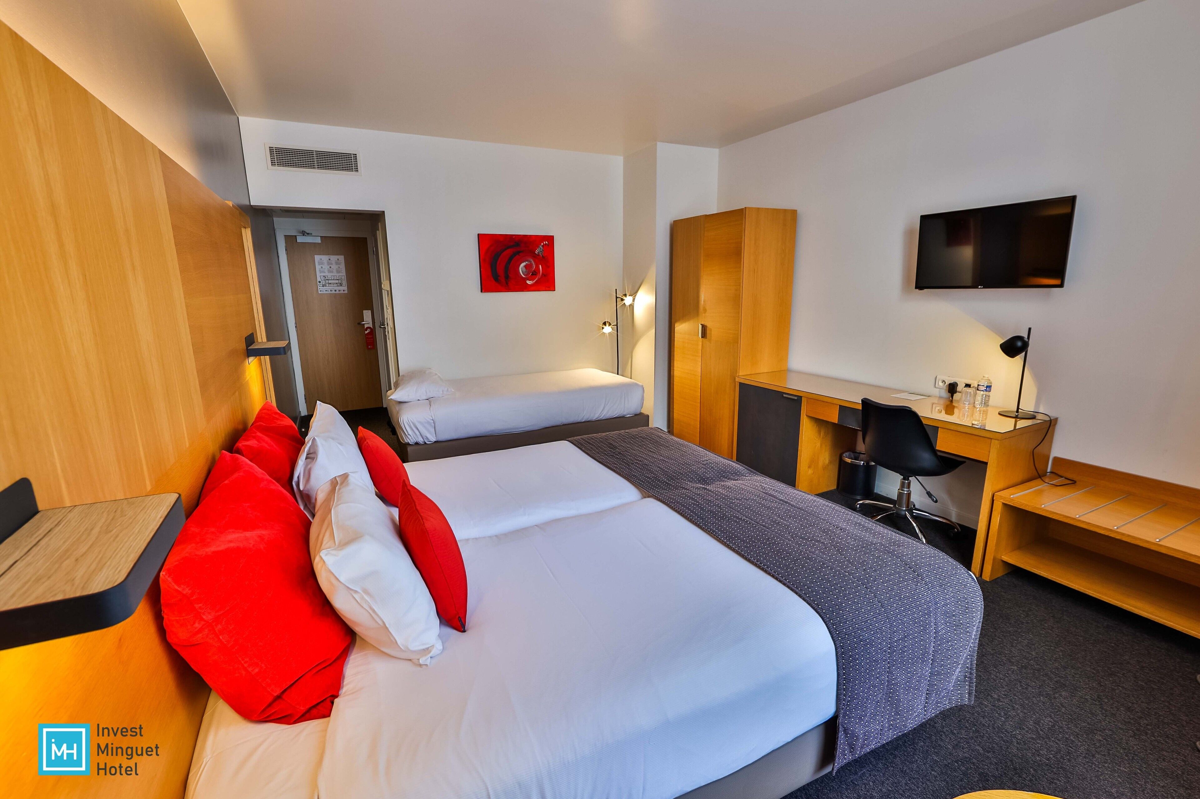 A hotel room with two beds, a desk, a chair, a TV, and a wardrobe.