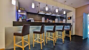 A bar area with four stools, a bar counter, a refrigerator stocked with beverages, and hanging pendant lights.