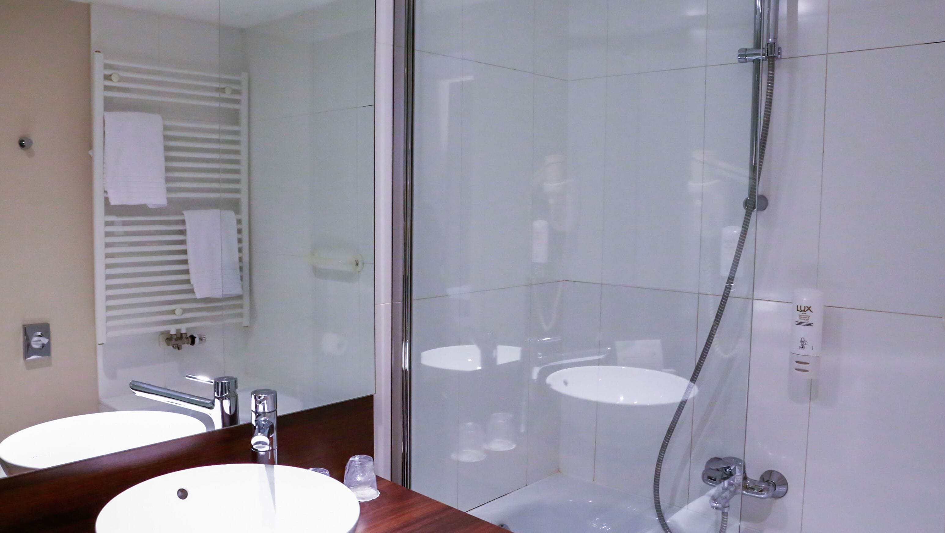 Un baño con ducha de mampara de vidrio, un lavamanos y un espejo.