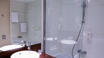 Un baño con ducha de mampara de vidrio, un lavamanos y un espejo.