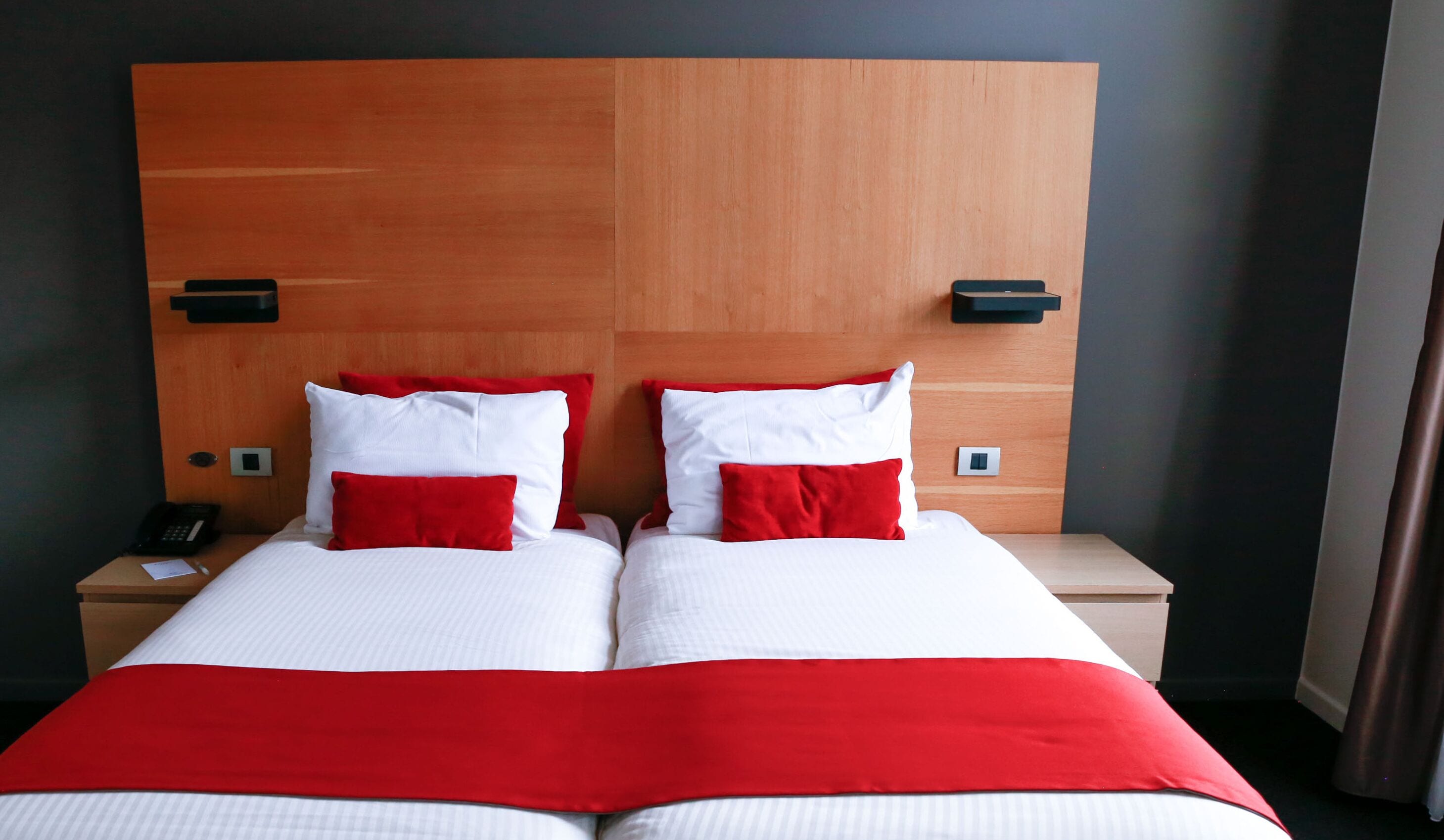 A hotel room with a wooden headboard, two beds with white and red bedding, bedside tables with black lamps, and a telephone on the left table.