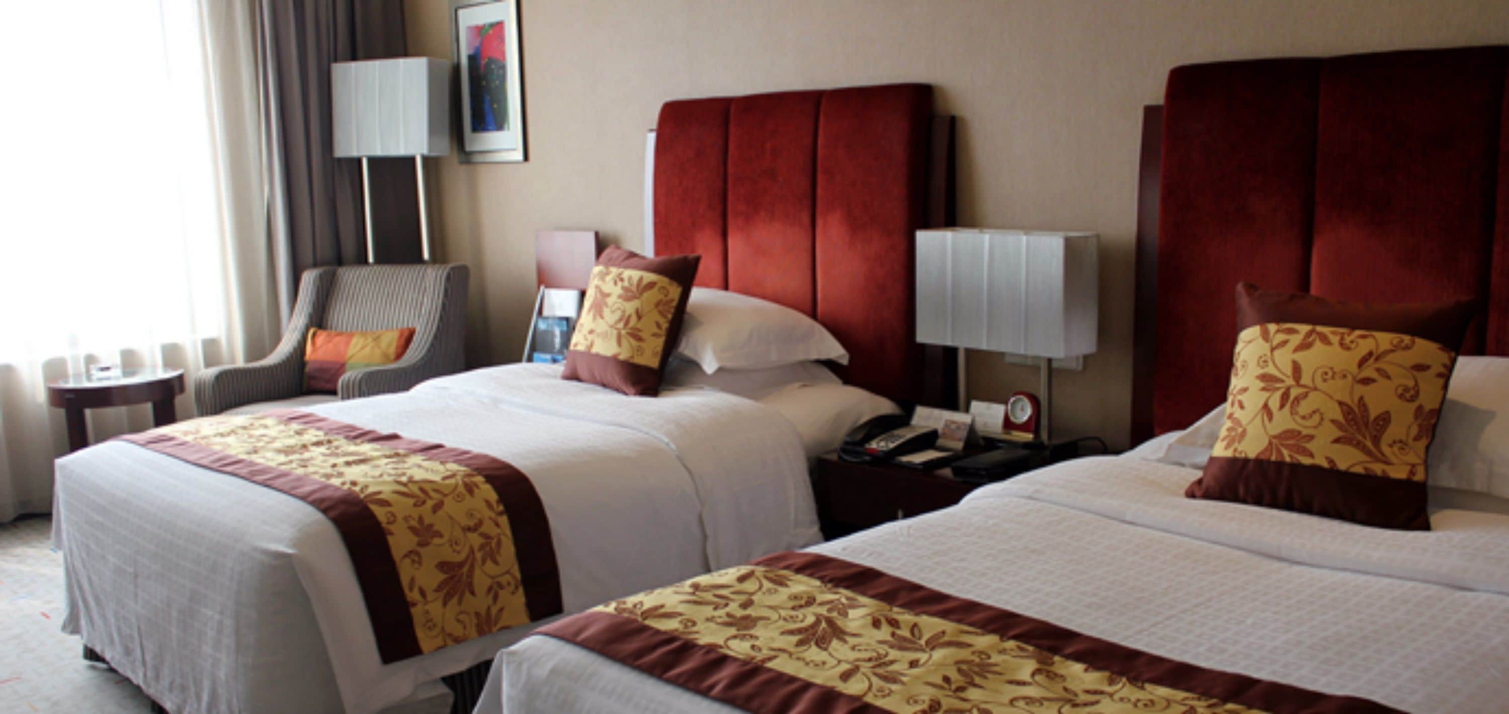 A hotel room with two beds, a chair, a nightstand, and a lamp.