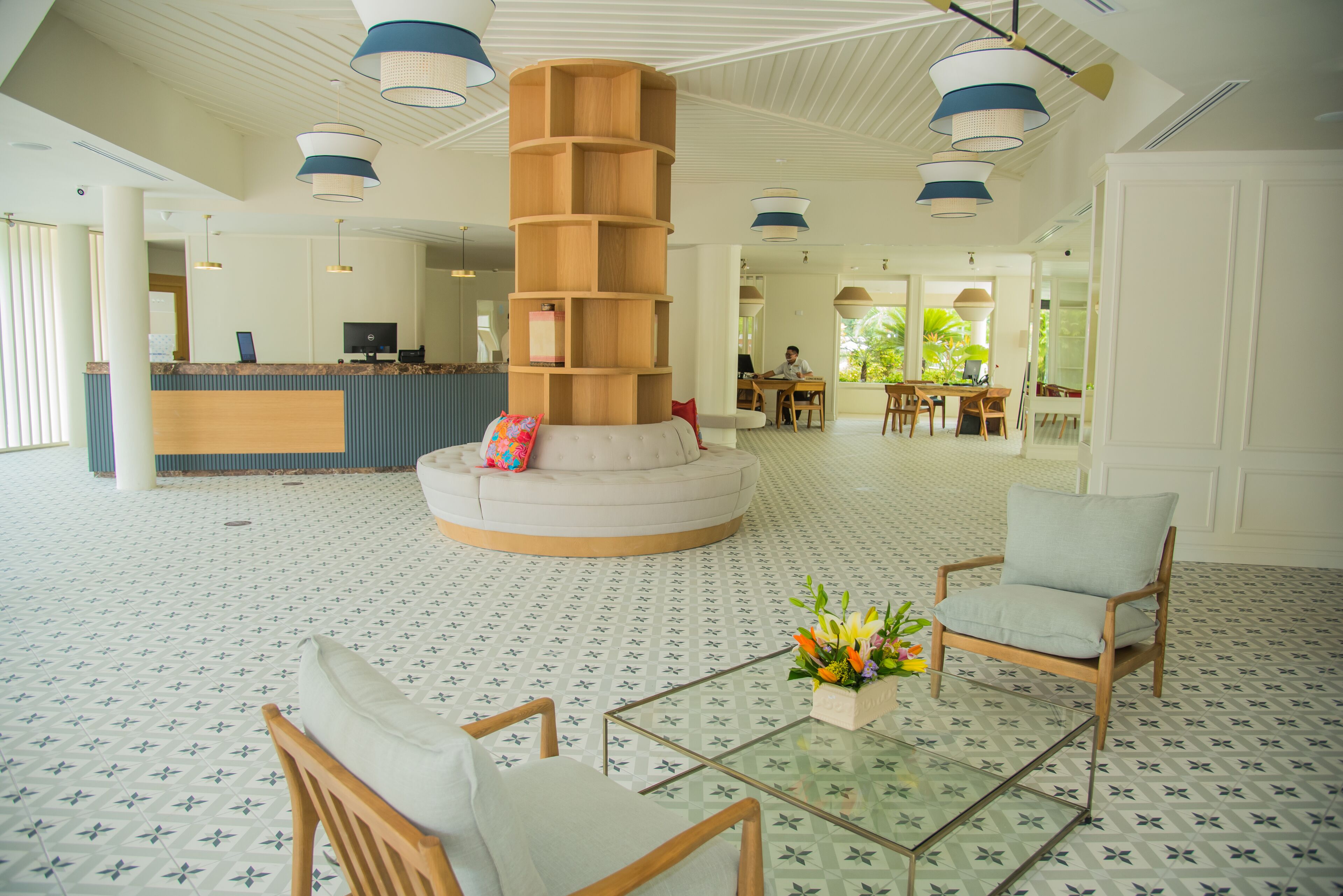 Vestíbulo con mostrador de recepción, un pilar central de madera, zona de estar y una mesa de centro de vidrio con flores.