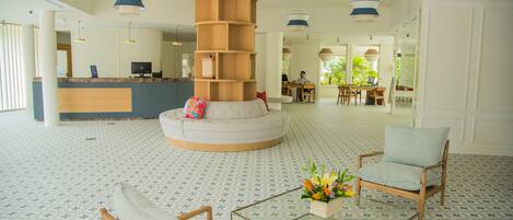 Vestíbulo con mostrador de recepción, un pilar central de madera, zona de estar y una mesa de centro de vidrio con flores.