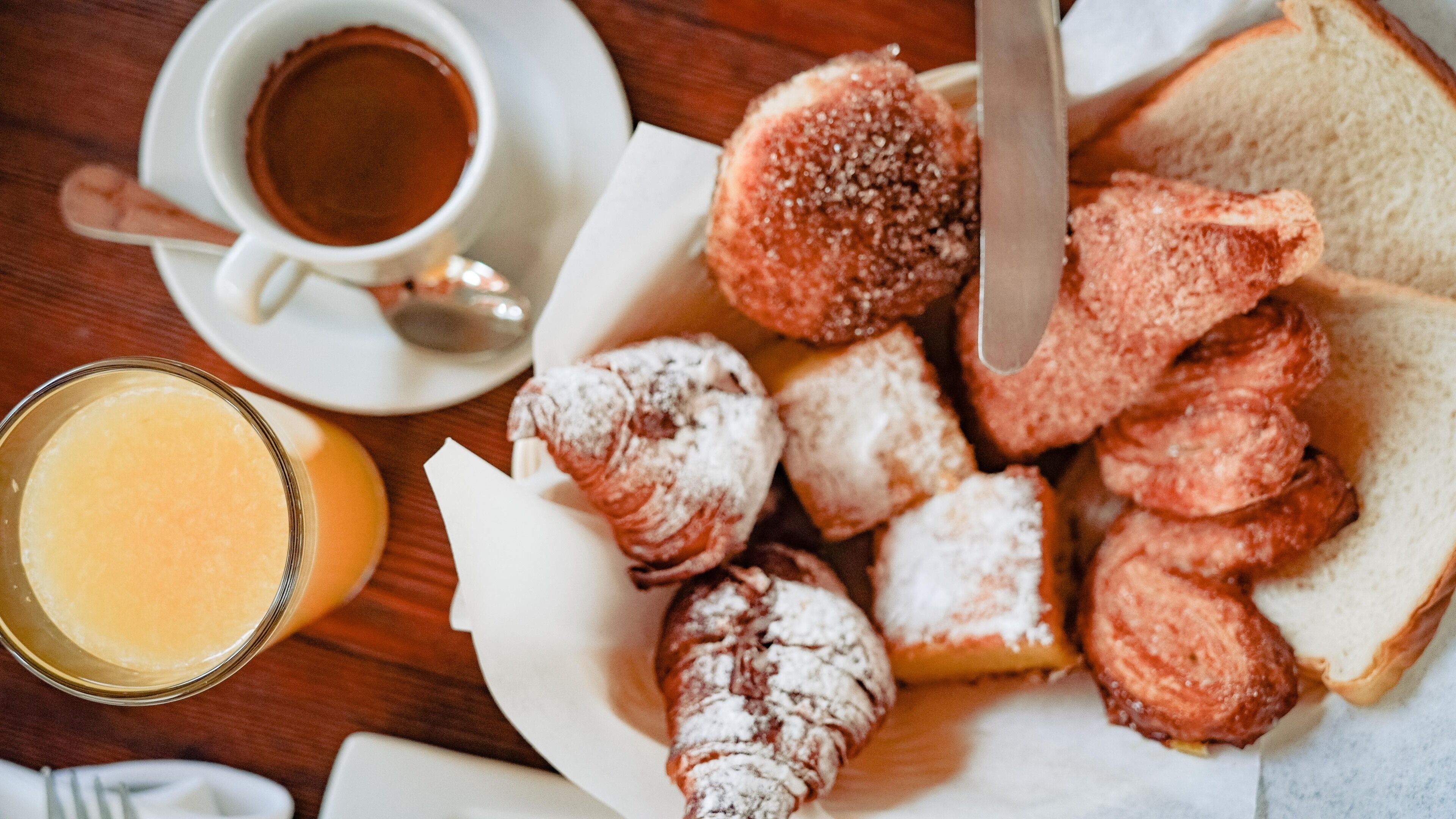 Un desayuno con pasteles, una taza de café y un vaso de zumo de naranja sobre una mesa de madera.