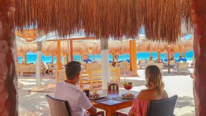 Un restaurante frente al mar con techos de paja, mesas y sillas de madera.