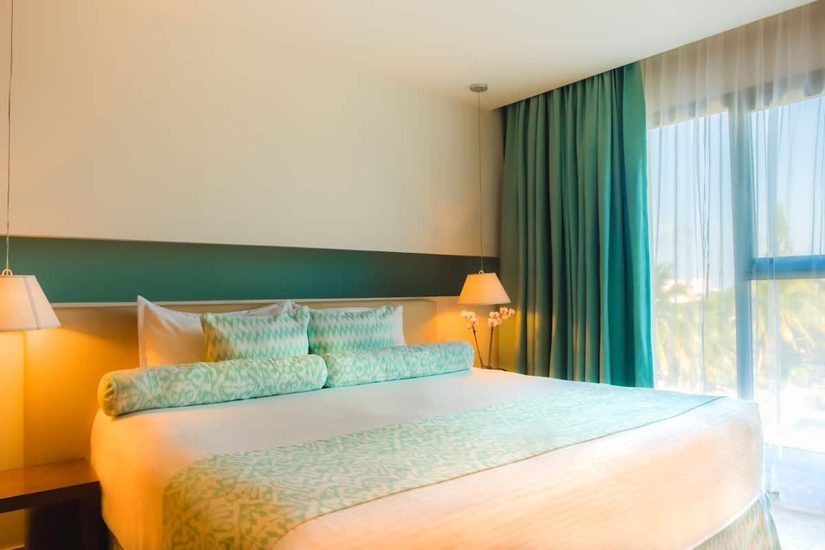 Ein Hotelzimmer mit einem großen Bett, zwei Nachttischlampen, einem Nachttisch und einem Fenster mit Vorhängen.