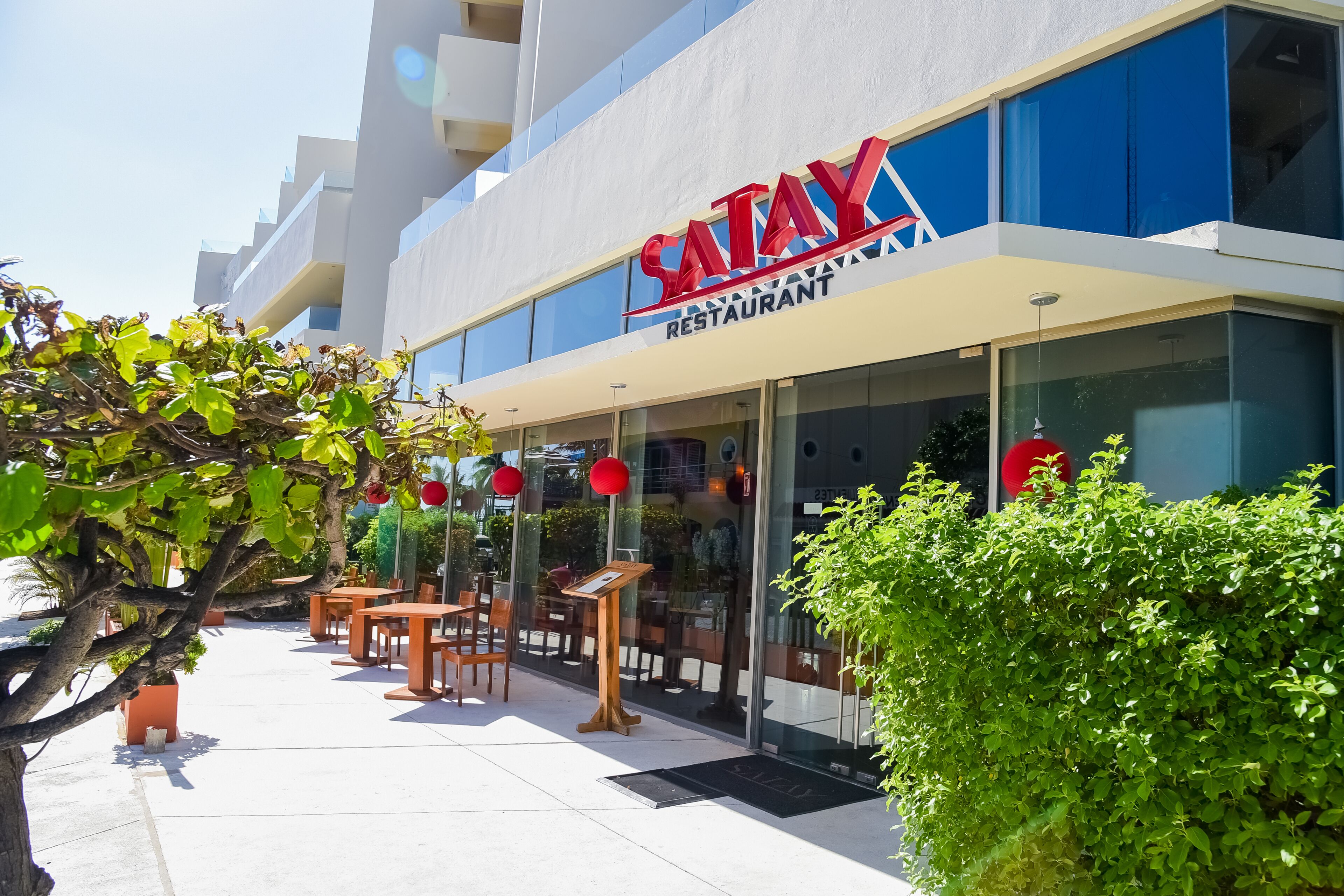 A modern restaurant with a clear sign, outdoor seating, and a well-maintained garden area.