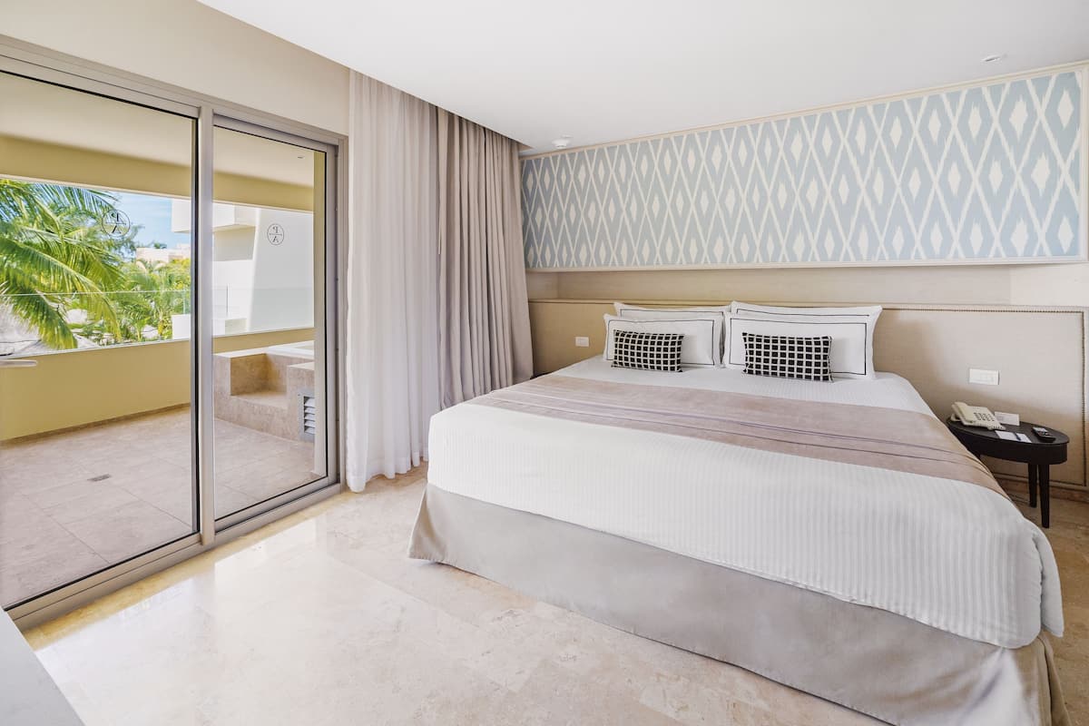Ein Hotelzimmer mit einem großen Bett, einem Balkon mit Blick auf Palmen und einer Wand mit Muster.