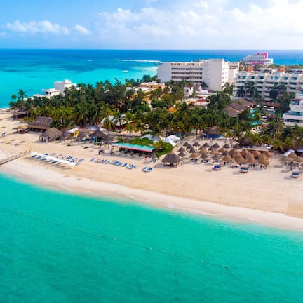 An aerial view of a beach resort with a pier, beach umbrellas, and a hotel with multiple floors.