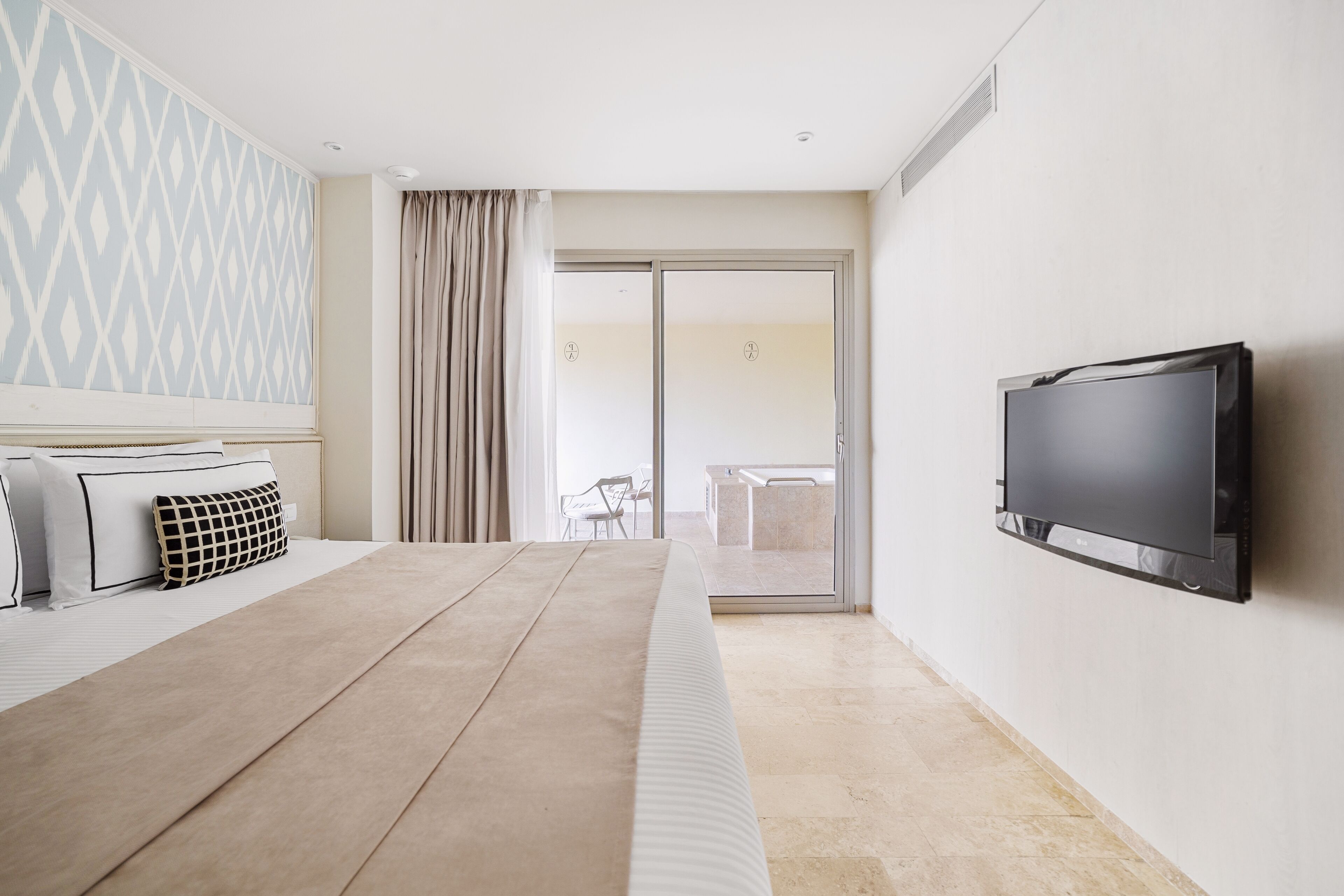 Ein modernes Hotelzimmer mit Bett, einem an der Wand befestigten Flachbildfernseher, einer Schiebetür zum Balkon und einem strukturierten Wanddesign.