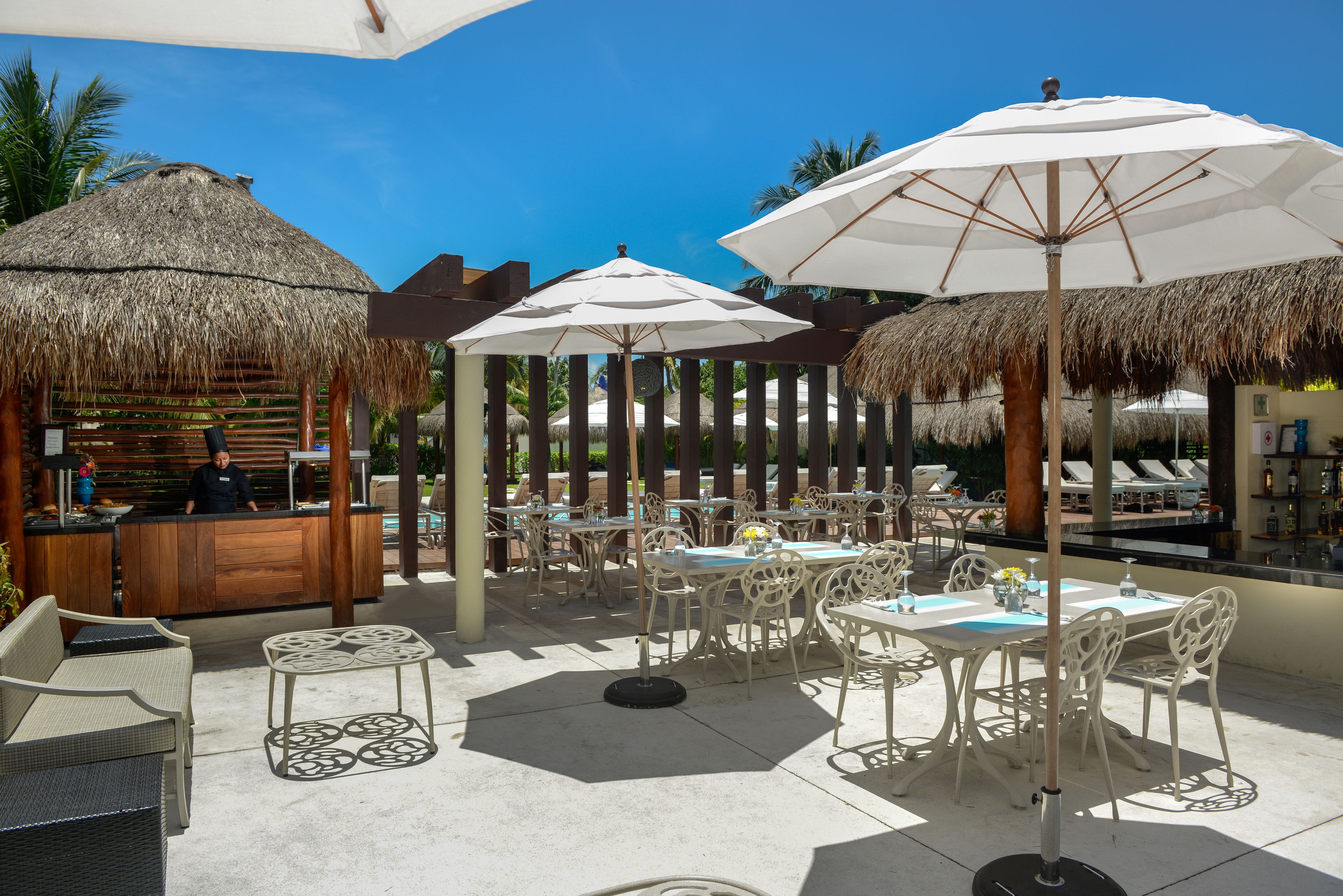 An outdoor dining area with thatched umbrellas, white chairs, and a bar counter.