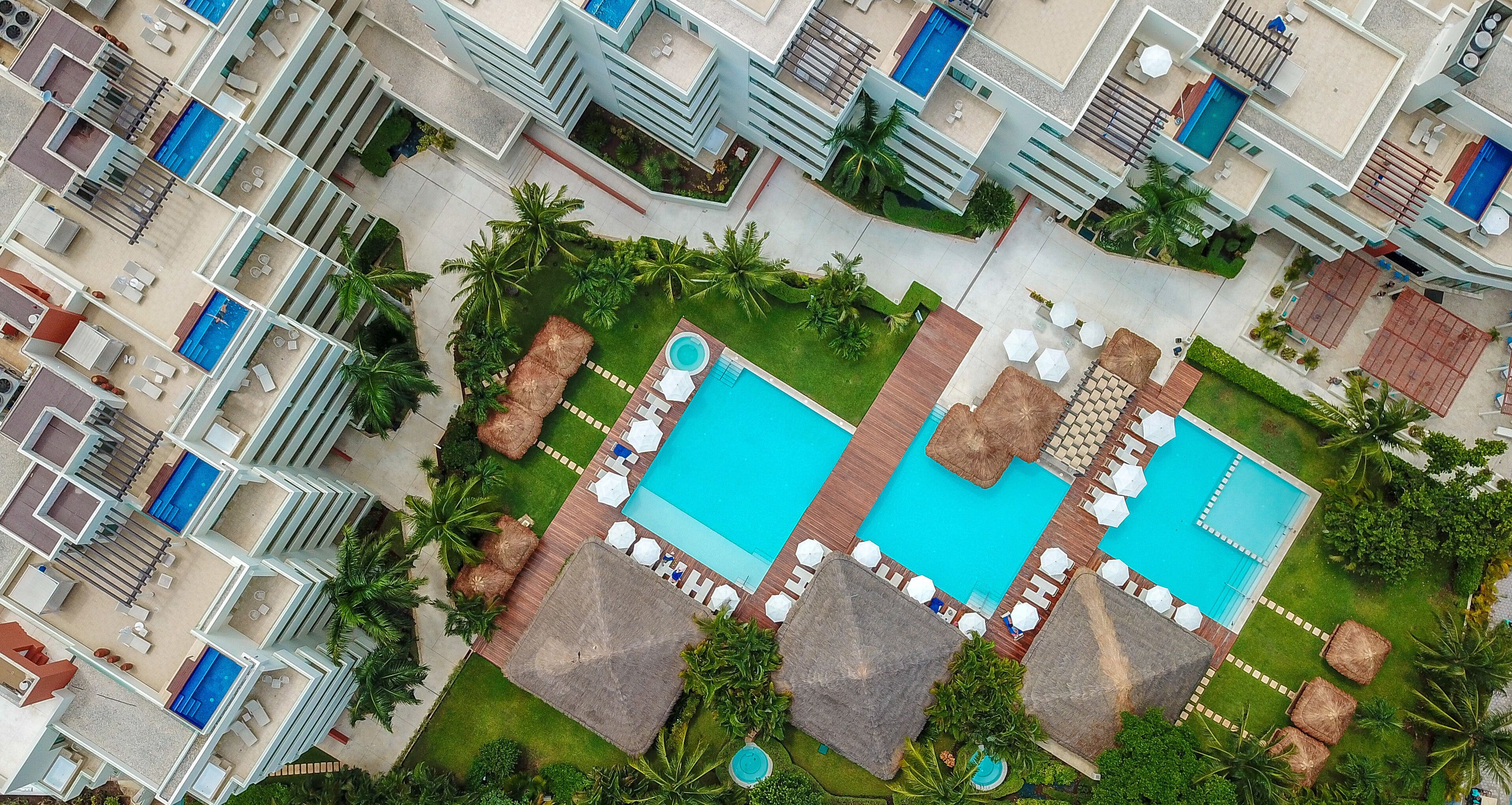 Vista aérea de un hotel con múltiples piscinas, zonas de estar al aire libre y abundante vegetación.