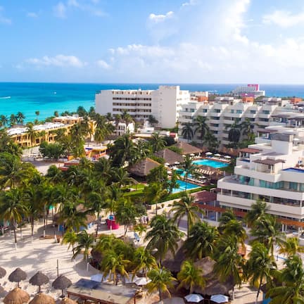 A resort with multiple buildings, a pool area, and a beach with umbrellas and palm trees.