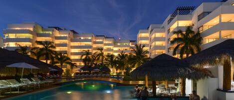 A hotel with multiple balconies, a swimming pool, and palm trees.