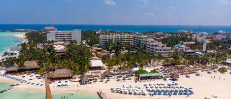 A coastal resort with a pier extending into turquoise waters, beachfront villas, and a sandy beach with umbrellas.