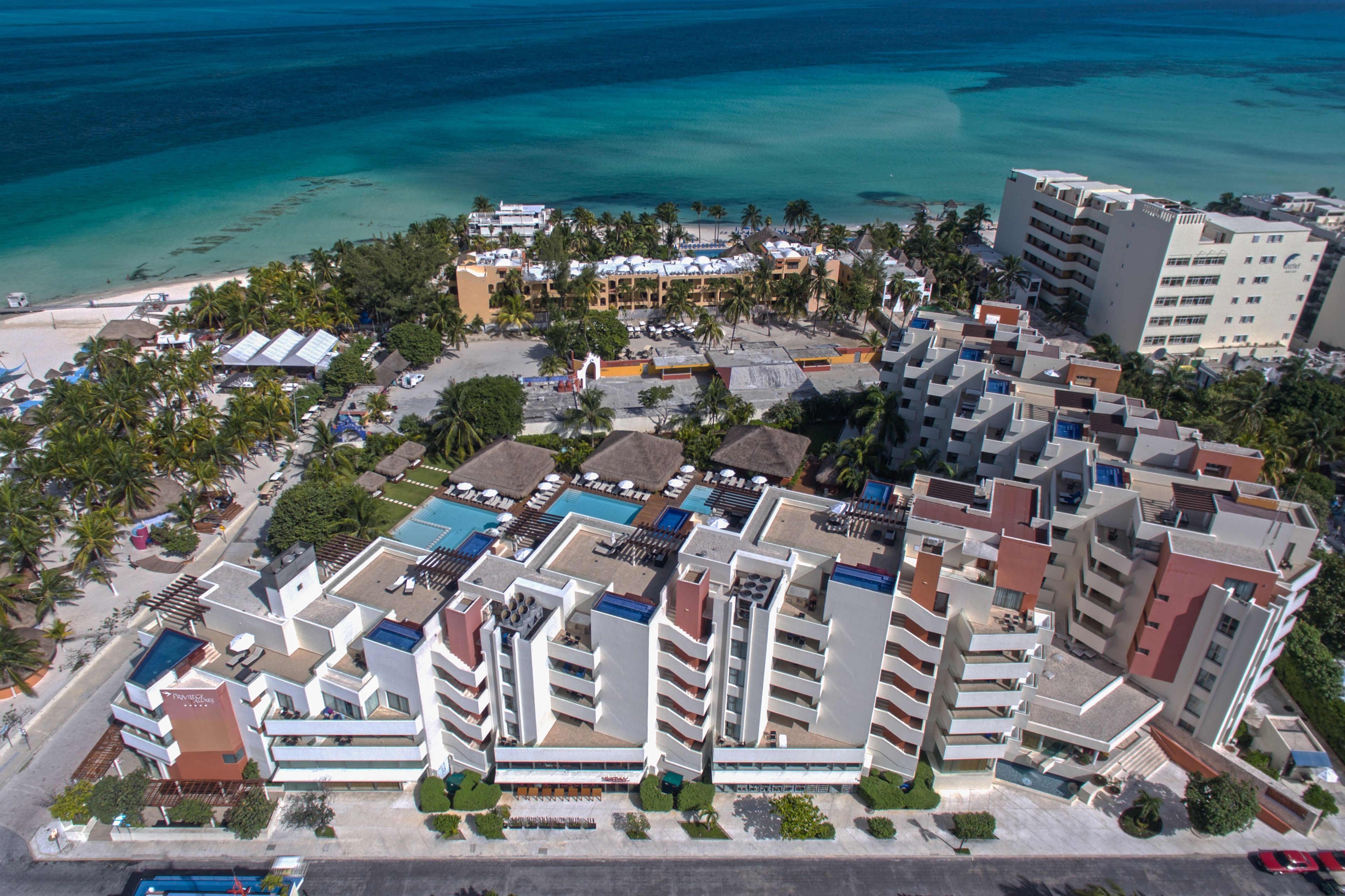 Vista aérea de un complejo turístico con varias edificaciones, una playa y un área de piscina.
