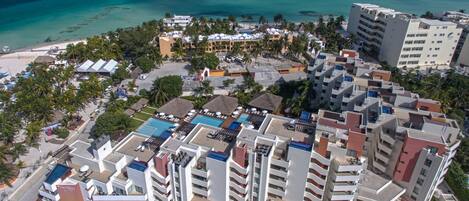 Vista aérea de un complejo turístico con varias edificaciones, una playa y un área de piscina.