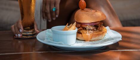 A plate with a burger and fries, a glass of beer, and a person sitting on a couch.