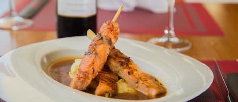 Un plato de salmón a la parrilla con patatas, una copa de vino tinto y una botella de vino sobre una mesa.