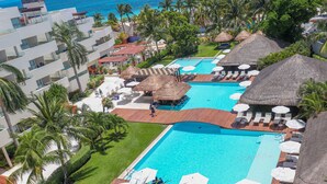 Un resort con varias piscinas, cabañas de techo de paja y palmeras.