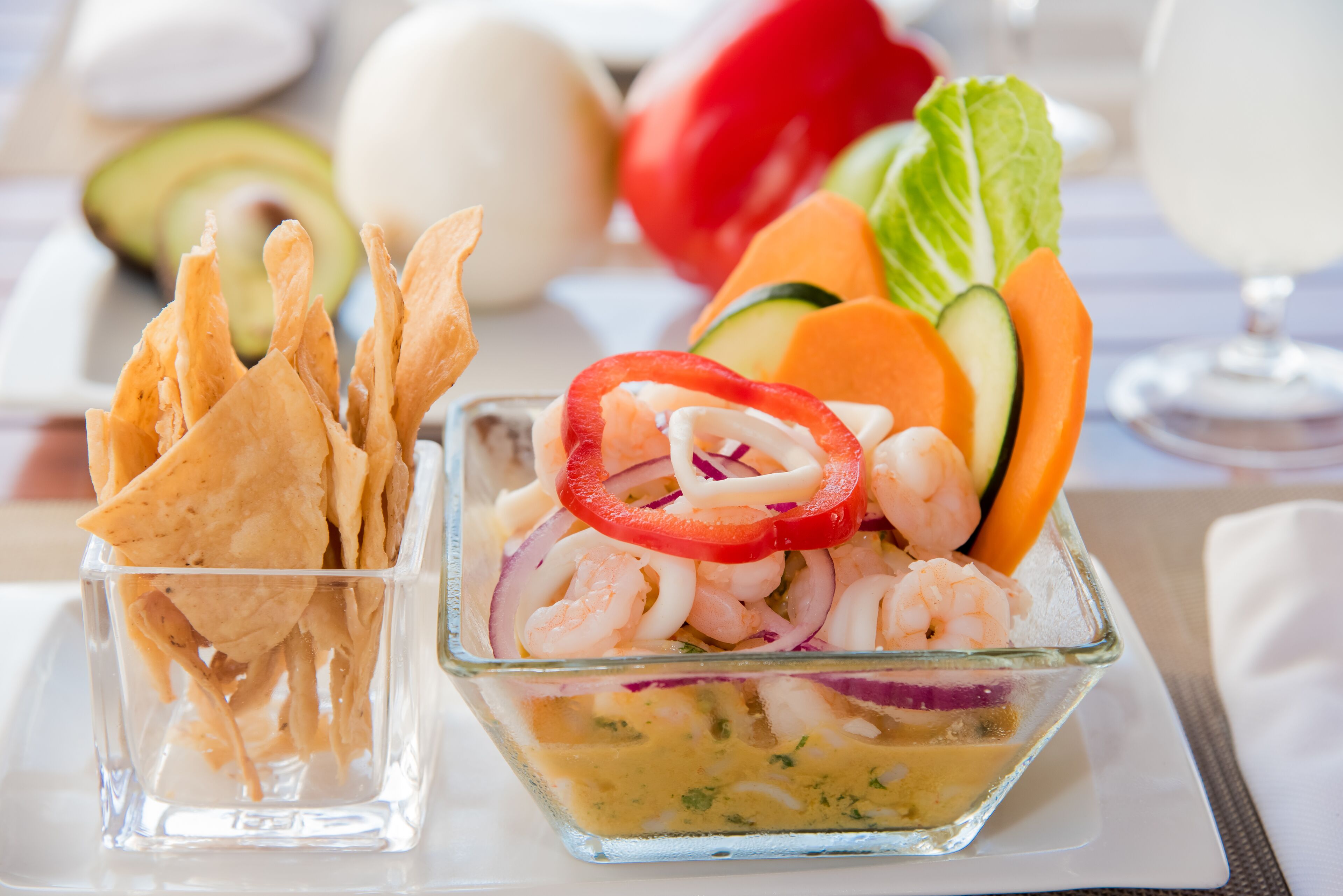 Un saladier en verre transparent contenant une salade de crevettes avec des légumes, et un verre séparé rempli de chips.