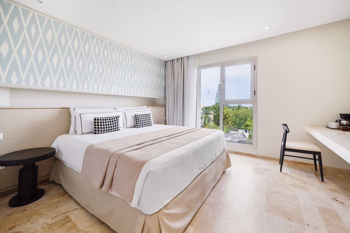 Ein modernes Schlafzimmer mit einem großen Bett, einem kleinen Tisch, einem Stuhl und Blick ins Grüne.