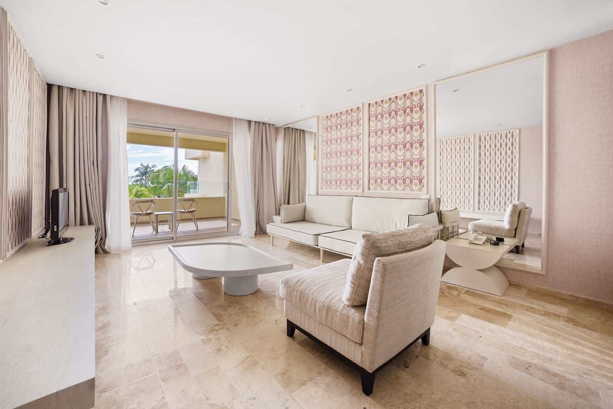 Ein geräumiges Wohnzimmer mit einer großen Couch, einem Couchtisch und einem Fernseher. Ein Balkon bietet Blick auf Palmen.