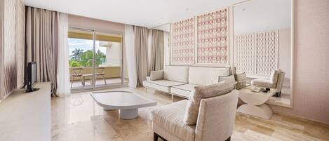 Un salón amplio con un sofá grande, una mesa de centro y un televisor. Tiene un balcón con vistas a palmeras.